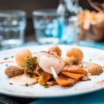 Prato elaborado com vieiras, legumes e batatas servido em um restaurante francês.