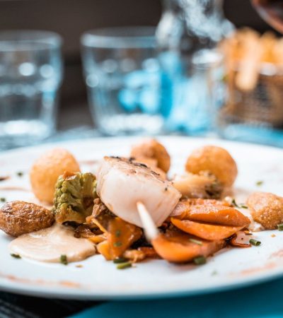Prato elaborado com vieiras, legumes e batatas servido em um restaurante francês.