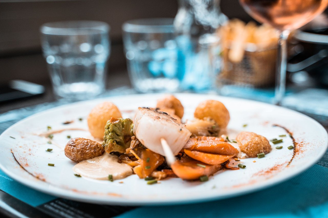 Prato elaborado com vieiras, legumes e batatas servido em um restaurante francês.