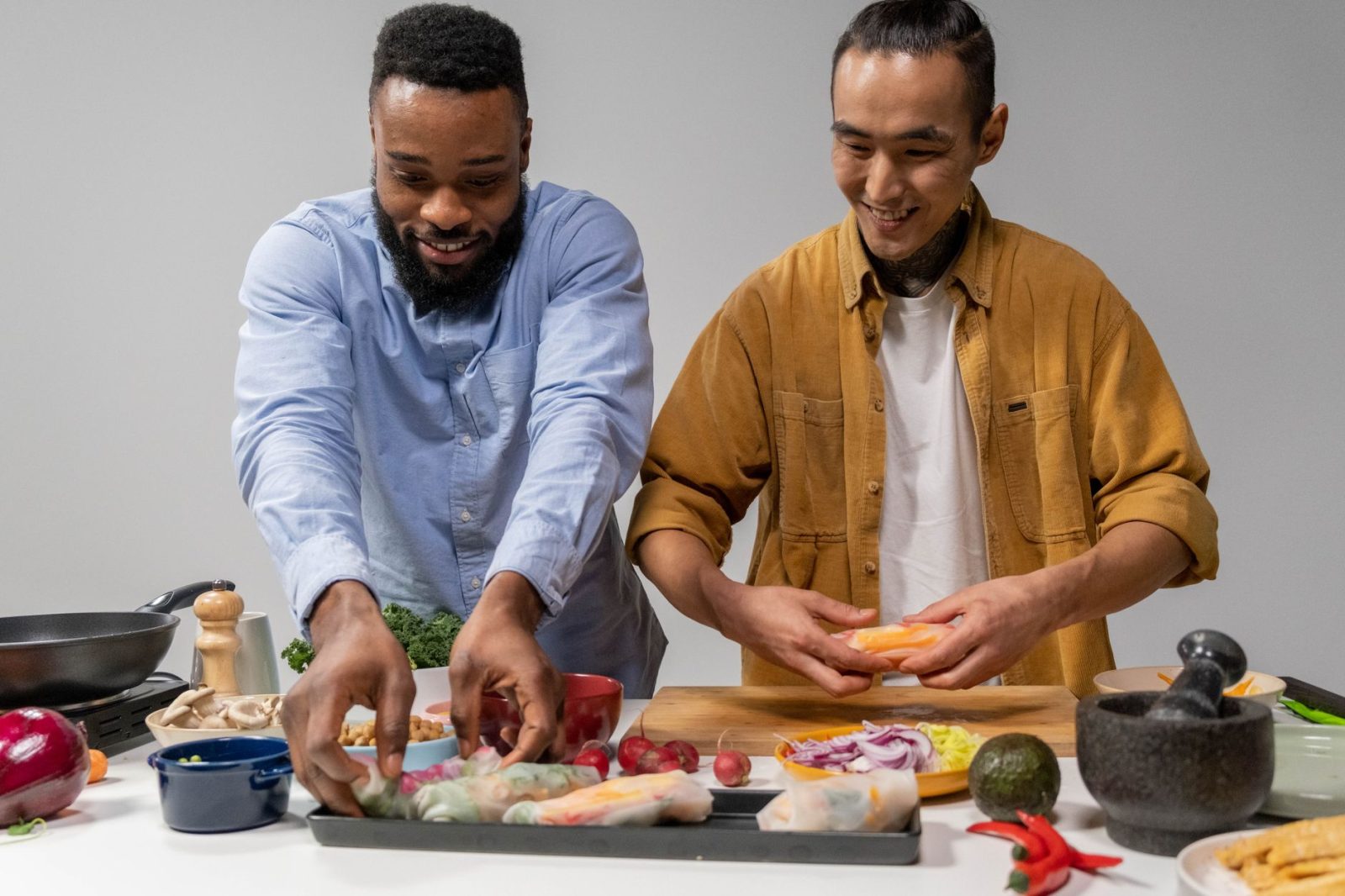 Duas pessoas preparam rolinhos primavera veganos em uma cozinha.