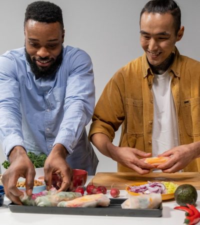 Duas pessoas preparam rolinhos primavera veganos em uma cozinha.