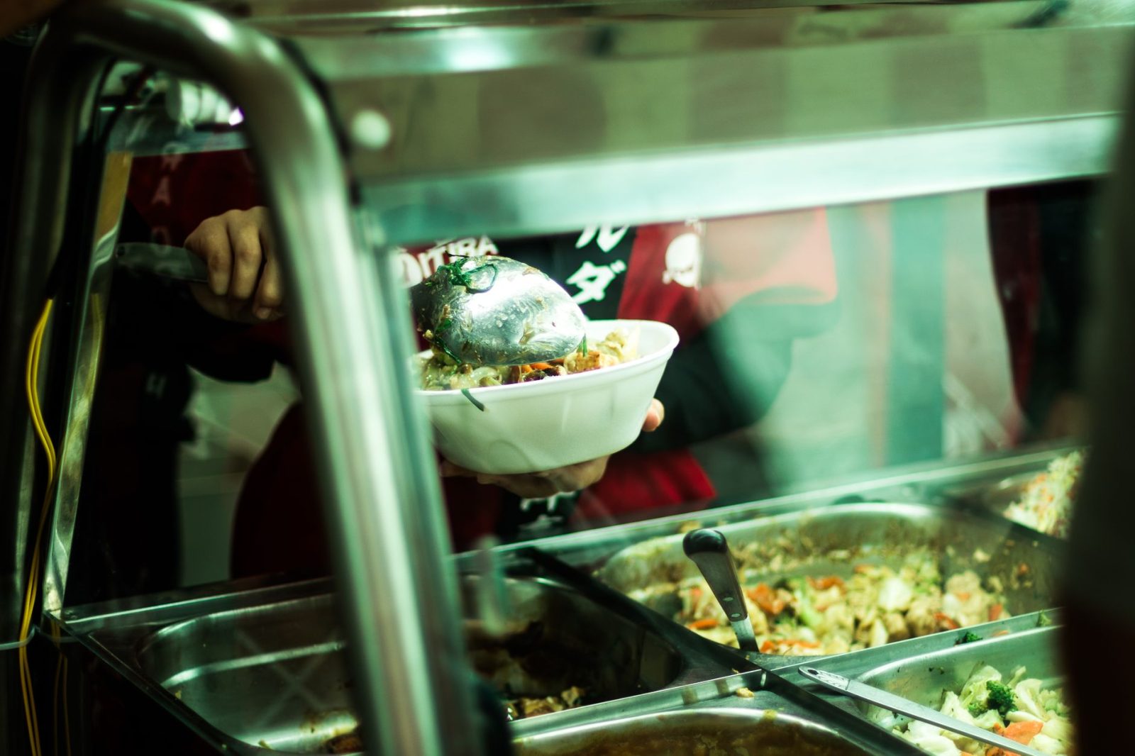 Pessoa servindo pratos variados em um balcão de comida brasileira.