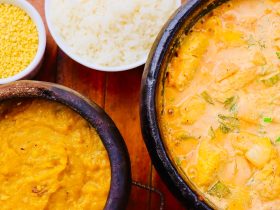 Moqueca brasileira colorida servida em panela de barro, acompanhada de guarnições sobre uma mesa de madeira.
