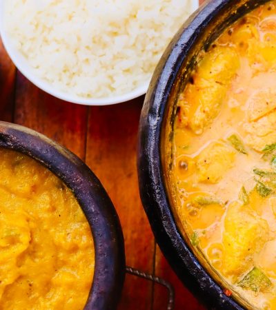 Moqueca brasileira colorida servida em panela de barro, acompanhada de guarnições sobre uma mesa de madeira.