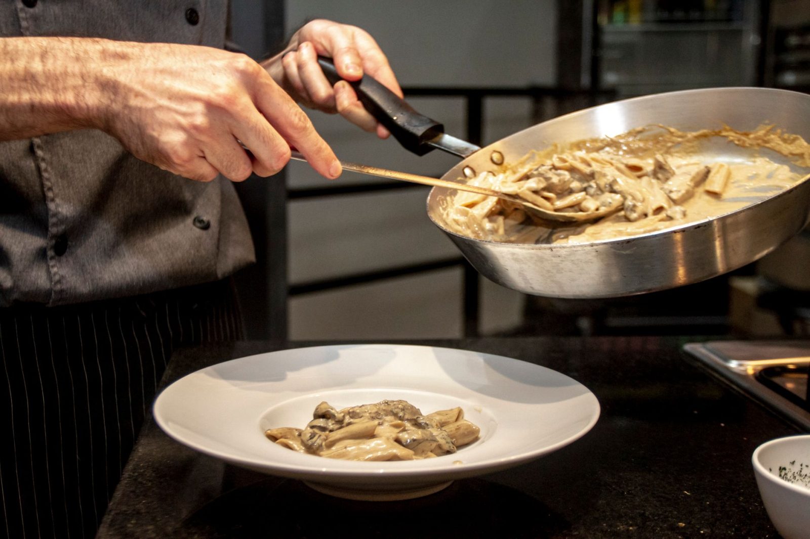 Chef finaliza a montagem de um prato de massa cremosa com cogumelos em uma cozinha.