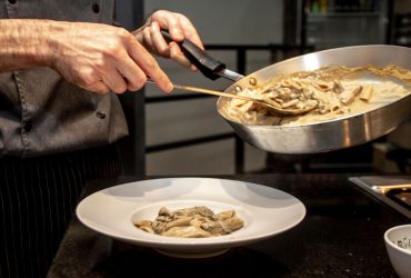 Chef finaliza a montagem de um prato de massa cremosa com cogumelos em uma cozinha.