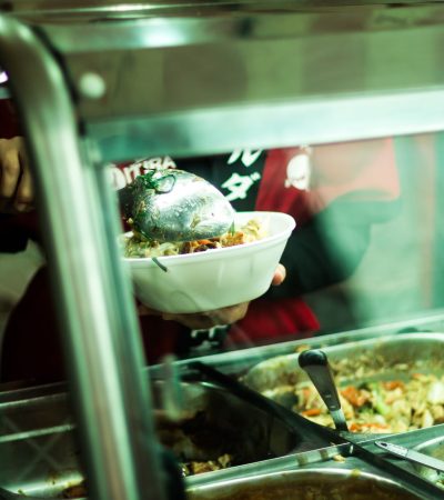 Pessoa servindo pratos variados em um balcão de comida brasileira.
